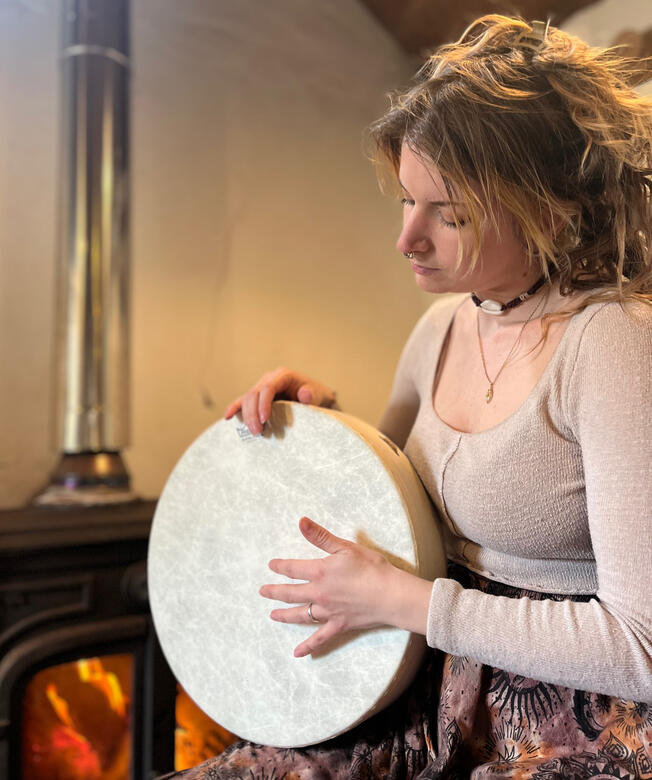 Untitled Image of Carli, birth doula, playing a hand drum by a fireplace